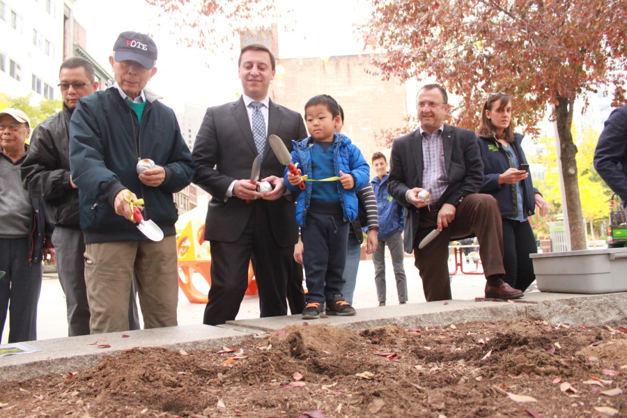 Chinatown community leader Frank Chin, State Senator Joe Boncore, and Greenway Board Chair Jim Kalustian help a young boy in Chinatown Park plant our 150,000th bulb!