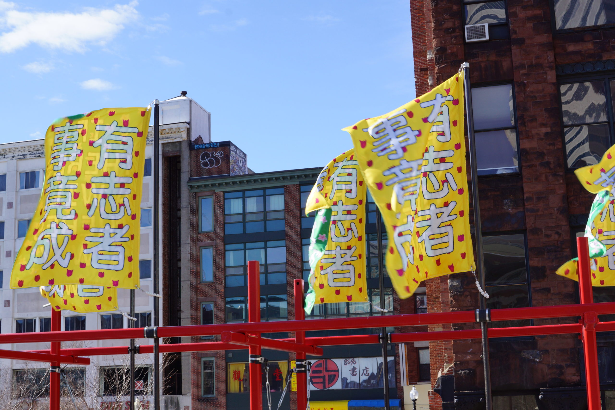 Four rectangular banners billow in the wind at the top of a red steel structure. Large white Chinese characters on the banners reads 