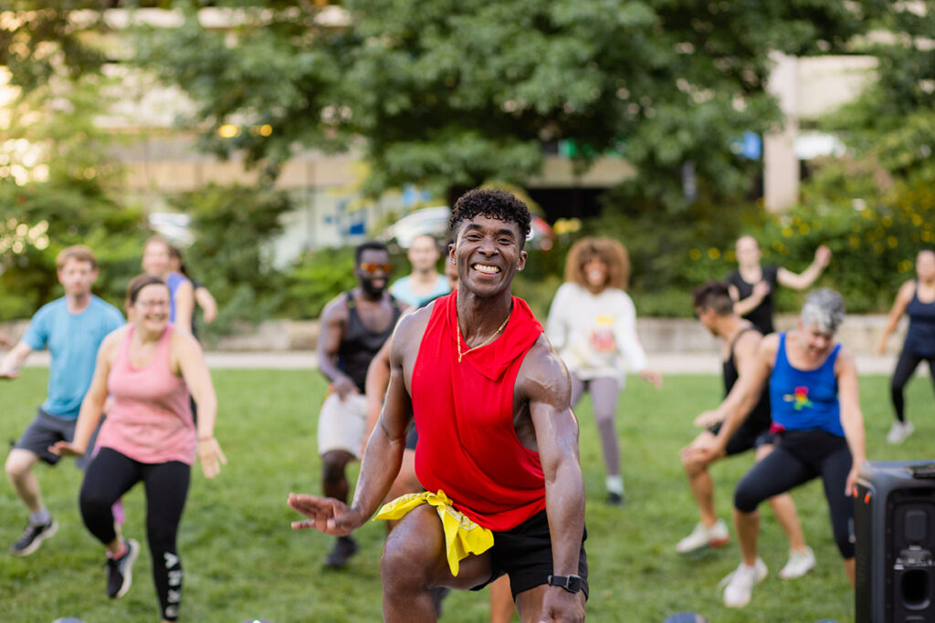 A fitness instructor smiles while leading an outdoor fitness class