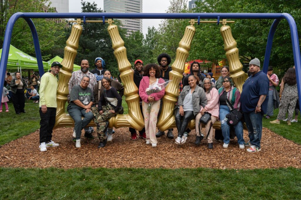 A group of people sits on and stands around two large swings, smiling at the camera.