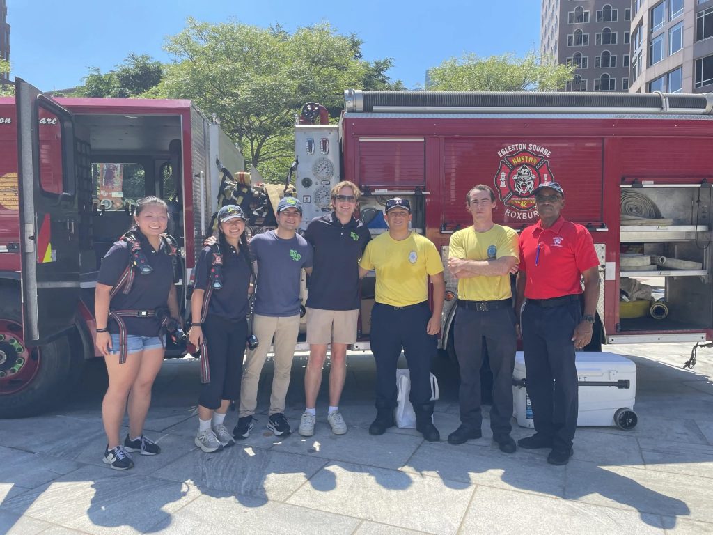 A group of people stand in front of a Roxbury fire truck, smiling at the camera.