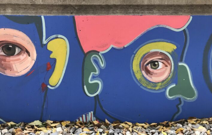 A mural of two faces with cartoon outlines and photorealistic eyes