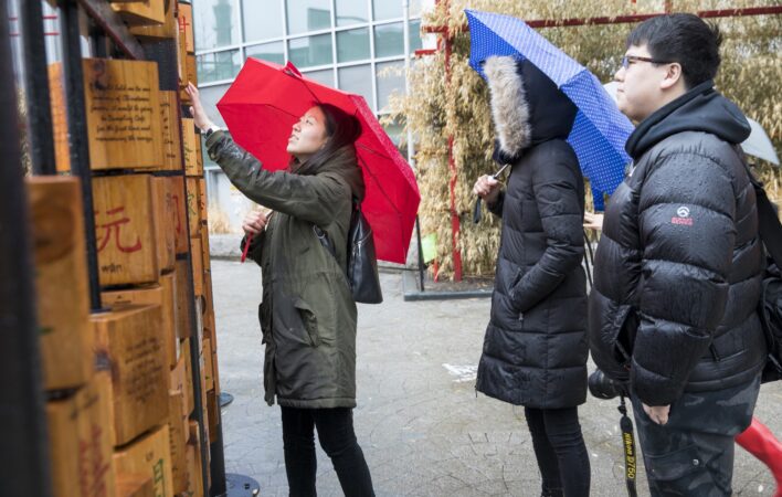 A woman with a red umbrella over her head reaches up to spin a wooden block on an abacus structure create by Risa Puno.